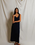 Woman wearing a navy blue dress standing against a plain white curtain.