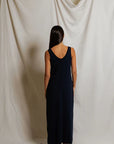 Woman wearing a long dark blue dress standing against a plain white curtain.