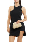 Woman wearing a black dress holding a beige clutch against a white background