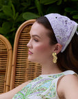 Woman wearing a decorative headband sitting on a wicker chair with greenery in the background