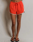 model wearing orange shorts with white trim against a beige background