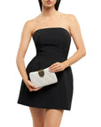 Woman wearing a black strapless dress holding a white clutch with a gold clasp on a white background