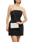 Woman in a black dress holding a white handbag with a gold chain strap on a white background