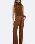 A woman modeling a brown sleeveless ribbed knit mock-neck top paired with matching brown wide-leg trousers, styled with tortoiseshell sunglasses and bracelets against a light gray studio background. full body front