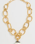 Gold chain bracelet with a black and white charm on a light gray background