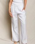 Person wearing white pants and a white top against a beige background