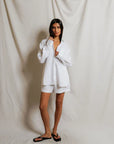 Person wearing a white robe and shorts against a plain background