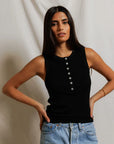 Woman wearing a black sleeveless top and blue jeans against a plain background