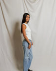 Woman wearing a white sleeveless top and light blue jeans against a plain background