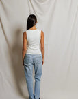 Person wearing a white sleeveless top and light blue jeans against a plain background