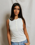 Woman wearing a white sleeveless top and blue jeans against a plain background