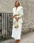 Woman in a white outfit with Martina Rope Clutch standing against a textured wall with a black metal gate.