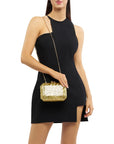 Woman wearing a black dress holding a gold handbag with shoulder strap on a white background
