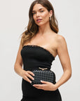 Woman holding a black woven handbag against a plain background