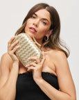 Woman holding a gold clutch against a plain background