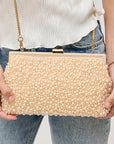 Gold pearl-handled clutch held by a person wearing a white top and blue jeans.