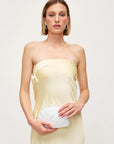Woman wearing a strapless yellow dress holding a white marble clutch against a plain background