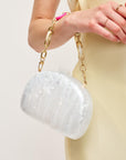 White textured handbag with gold chain strap held by a person wearing a yellow dress.