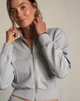 Woman wearing a gray zip-up hoodie and matching pants against a plain background