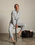 Woman in gray outfit sitting on a stool with a duffel bag in the background.
