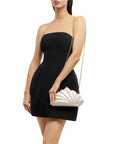 A woman modeling a strapless black mini dress, holding a white scalloped clutch bag with a gold chain strap against a plain white background.