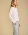 A woman in a white long-sleeve top and light gray sweatpants, shown in profile against a solid beige studio background.