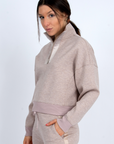 Woman wearing a light gray zip-up sweatshirt and pants on a white background side view