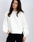 Woman wearing a white sweater and black pants against a plain background front view