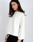 Woman wearing a white sweater against a plain background