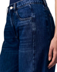 Close-up of dark blue denim jeans worn by a model, showing the front and side pockets with a hand resting on the thigh.