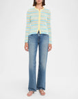 A model wearing a light blue and yellow striped knit cardigan with a yellow zipper, paired with blue jeans and pink sandals, against a plain white studio background.