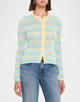 A woman wearing a light blue, yellow, and white striped knit cardigan with blue jeans, shown from the neck down against a plain white background.