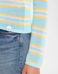 Close-up of a model wearing a light blue open-knit long-sleeve top with yellow and white horizontal stripes, paired with blue jeans.