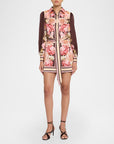 A model wears a long-sleeved mini dress featuring a pink and beige floral print on the body, combined with solid dark brown sleeves and striped details, paired with black strappy high-heeled sandals against a light gray studio background.
