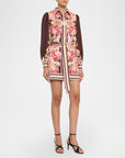 A model wears a long-sleeved mini dress featuring a pink and beige floral print on the front panel and a contrasting solid dark brown sheer long sleeve. The dress has a matching tie belt at the waist and is paired with black strappy high-heeled sandals against a plain white studio background.