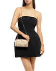 A woman wearing a black strapless mini dress and holding a small rectangular clutch with a gold chain strap. The clutch has a marbled beige and white pattern.