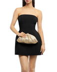 A woman wearing a strapless black mini dress and holding a metallic gold textured clutch bag against a plain white background.