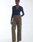 A model stands against a plain white studio background wearing a navy and gold striped long-sleeve polo shirt, olive green wide-leg cargo pants, and brown pointed-toe heels.
