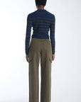 A model shown from the back wearing a navy blue long-sleeve knit top with thin mustard yellow stripes and olive green wide-leg cargo pants, set against a plain white studio background.