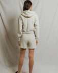 model wearing a zip up hoodie and lounge shorts in the color oatmeal, back view