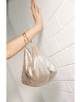 Gold mesh handbag held by a hand against a light tiled wall.