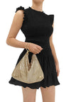 Black dress with ruffled details worn by a person holding a gold bag on a white background