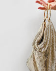 Gold mesh handbag held by a hand against a light gray background