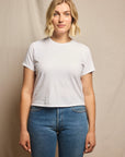 Woman wearing a plain white t-shirt and blue jeans against a beige background, size L