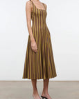 A woman modeling a sleeveless midi dress with vertical brown and olive-gold stripes, paired with black strappy heeled sandals, against a plain white studio background.