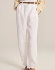 Person wearing white pants with a beige sweater on a plain background