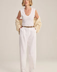 Woman wearing a white sleeveless top and pants with a beige cardigan on a plain background