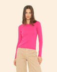 Woman wearing a bright pink sweater and beige pants on a beige background