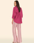 Woman wearing a pink top and striped pants on a beige background back view