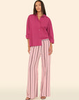 Woman wearing a pink shirt and striped pants on a beige background front view